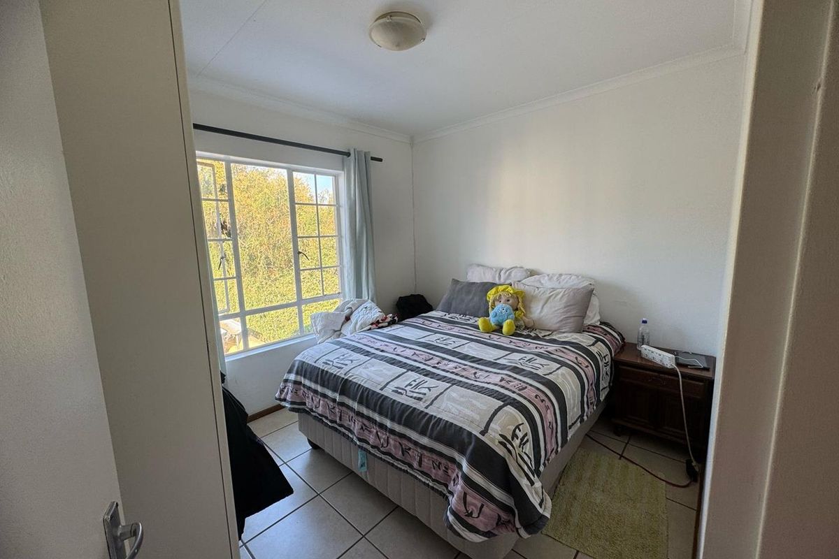 A functional bedroom featuring tiled flooring and a large window that provides natural light and a view of the surrounding greenery.