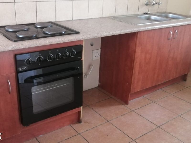 A functional kitchen featuring wooden cabinetry, laminate countertops, a built-in oven with electric hob, and a double bowl sink with tiled backsplash.