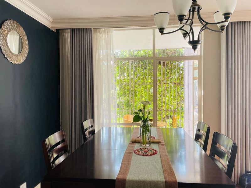 A well-lit dining room featuring crown molding, a classic wrought iron chandelier, and large windows providing natural light and garden views.