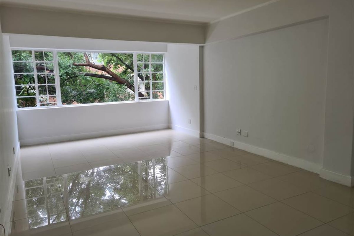 A bright, spacious, and empty living area featuring polished large-format floor tiles and a large multi-pane window with a leafy green outlook.
