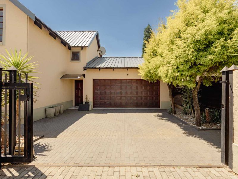 Front exterior view of the townhouse featuring a paved driveway, secure metal gate, and a single-car garage with a metal roof.