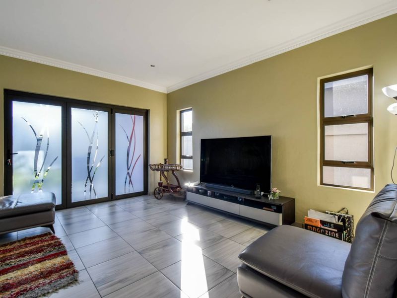 A well-lit living room featuring large tiled floors, decorative sliding glass doors, and multiple windows providing natural light.