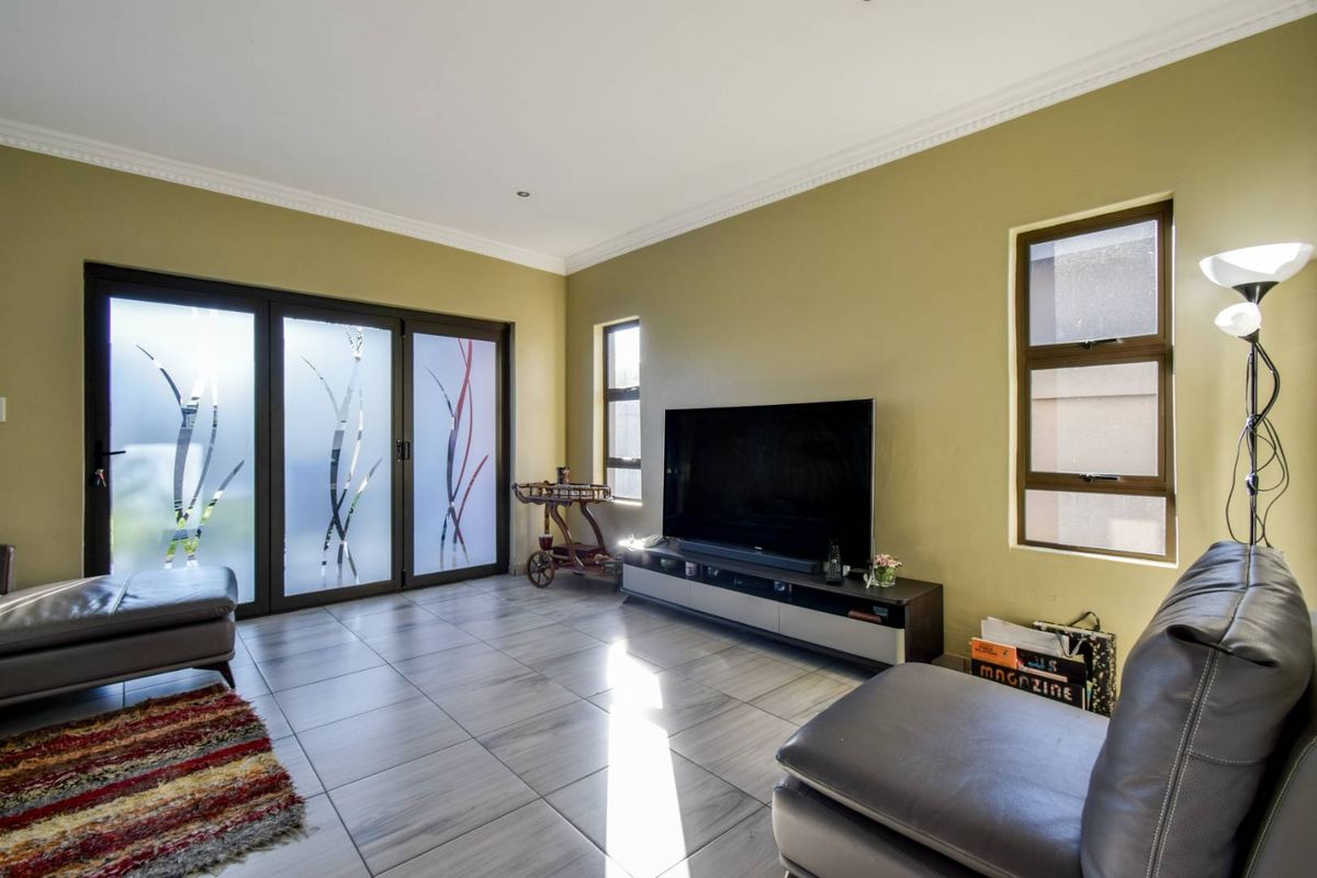 A well-lit living room featuring large tiled floors, decorative sliding glass doors, and multiple windows providing natural light.