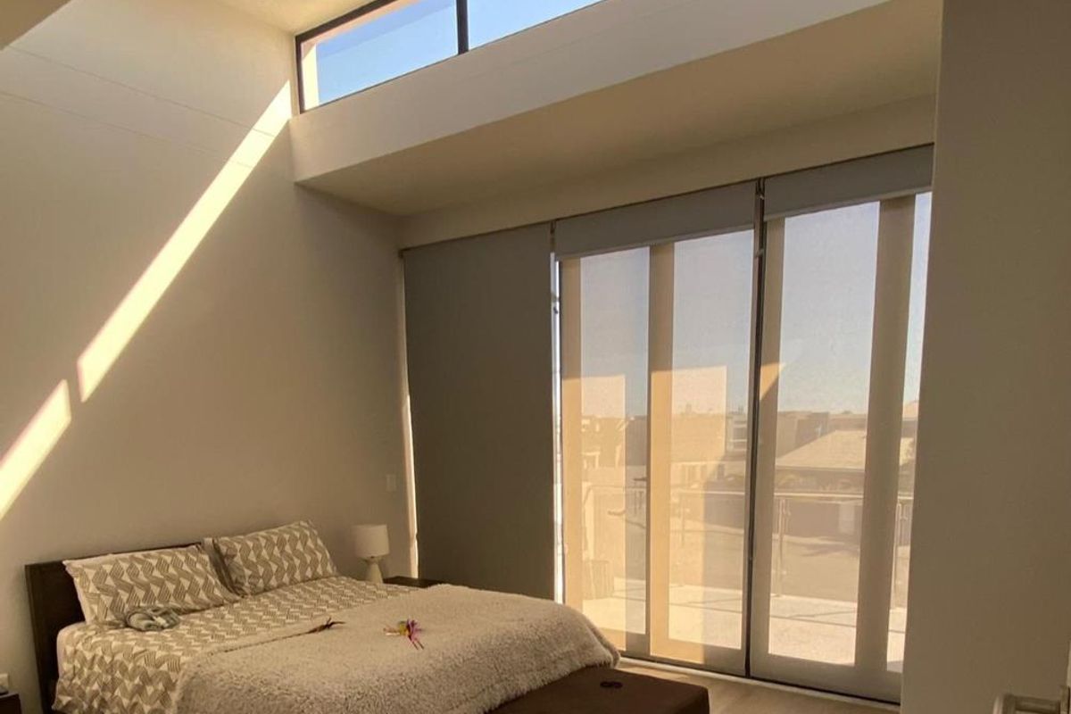 Bright and airy bedroom featuring high ceilings with clerestory windows and large sliding glass doors providing access to an outdoor balcony.