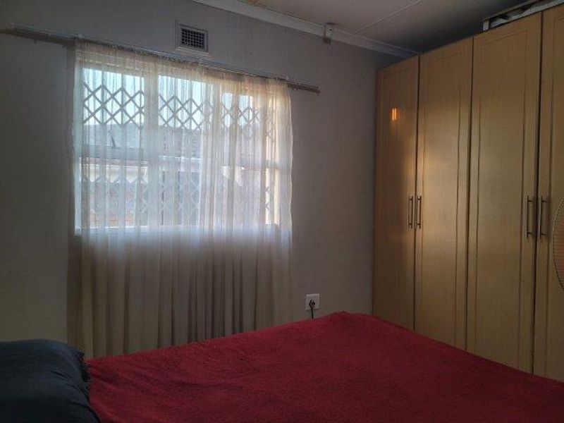 A bedroom featuring built-in wooden cupboards and a window fitted with a security gate.
