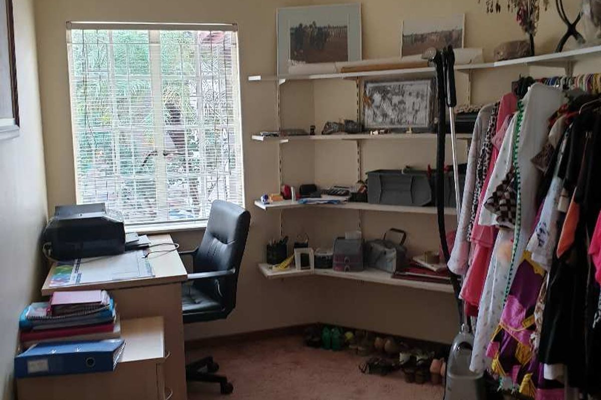 A functional bedroom or home office space featuring wall-mounted shelving units and a window with security bars.