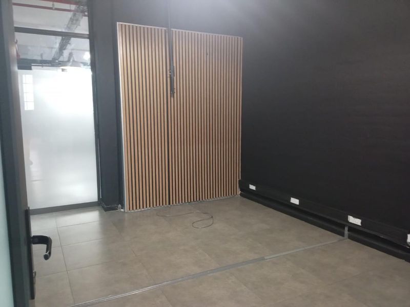 A modern, empty office space featuring contemporary slatted timber wall paneling, large format floor tiles, and a sleek frosted glass entrance door.