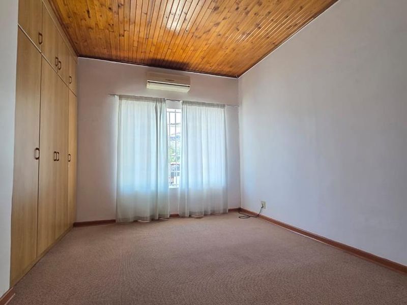 A spacious bedroom featuring built-in cupboards, a timber-paneled ceiling, carpeted flooring, and a wall-mounted air conditioning unit.