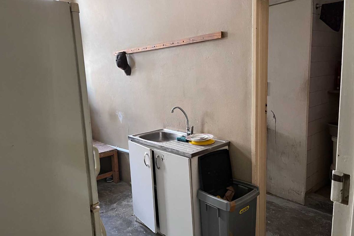 A basic industrial kitchen area featuring a single stainless steel sink unit with base cabinetry and access to an adjacent utility space.
