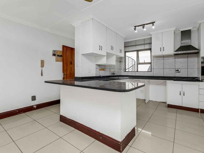 A functional kitchen featuring granite countertops, built-in cabinetry, a stainless steel extractor fan, and tiled flooring, offering a clean and practical workspace.