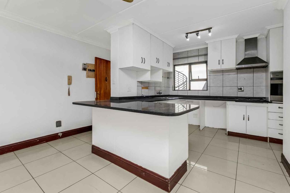 A functional kitchen featuring granite countertops, built-in cabinetry, a stainless steel extractor fan, and tiled flooring, offering a clean and practical workspace.