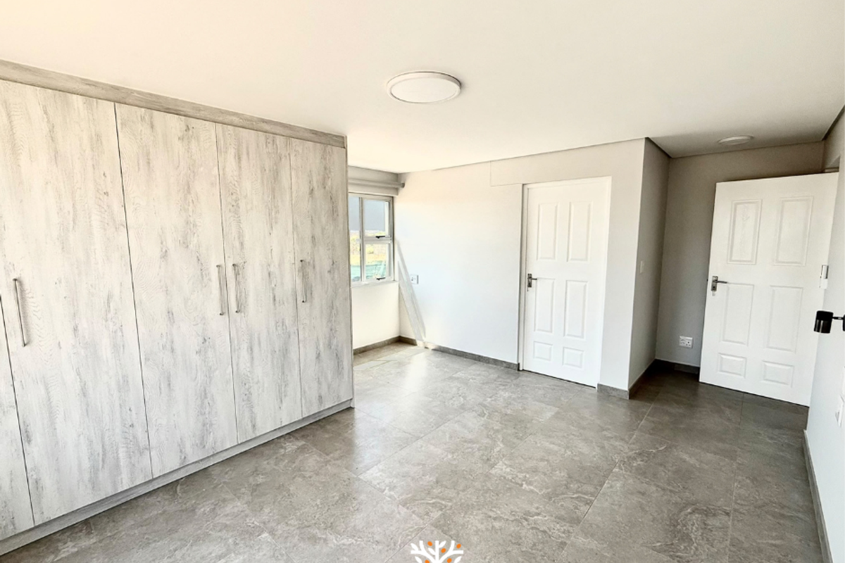 A bright, modern bedroom featuring neutral tiled flooring, built-in wooden cupboards, and clean white walls, offering a versatile space ready for personalization.