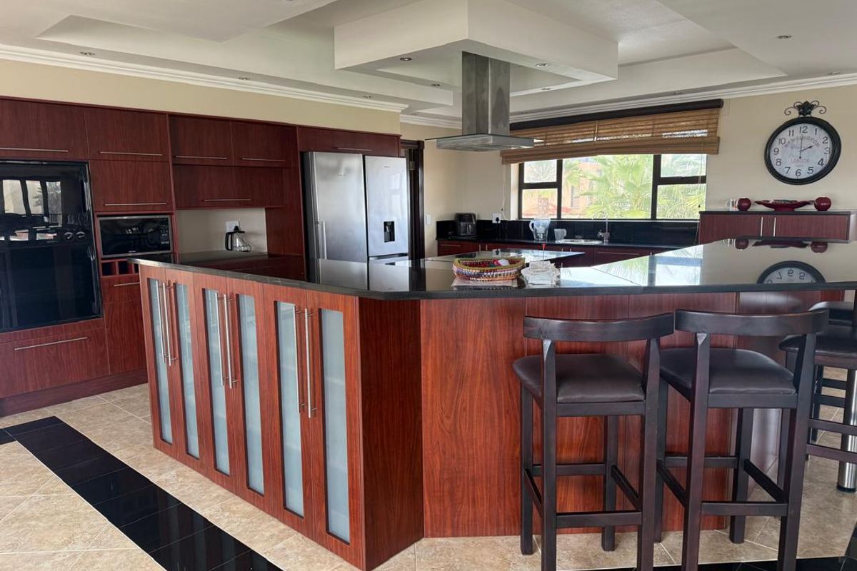 Spacious kitchen featuring dark wood cabinetry, a large central island with stone countertops, integrated appliances, and modern recessed lighting.