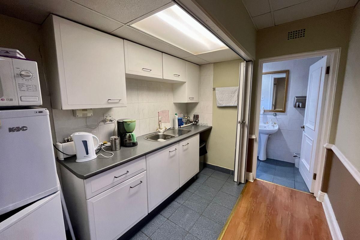 Compact kitchenette featuring white cabinetry, stainless steel sink, and tiled backsplash, with direct access to an adjacent bathroom.