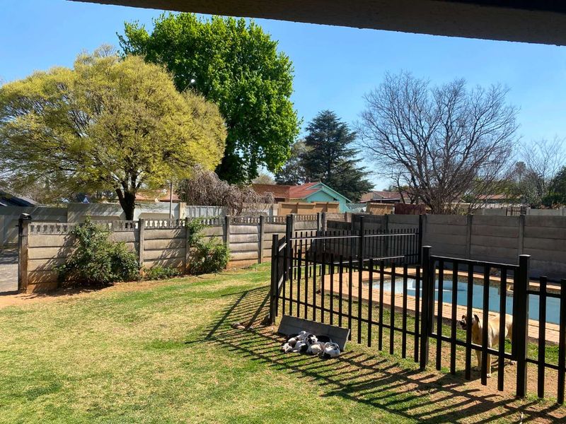 A backyard area featuring a swimming pool enclosed by a black metal safety fence, set within a lawn with precast concrete boundary walls.