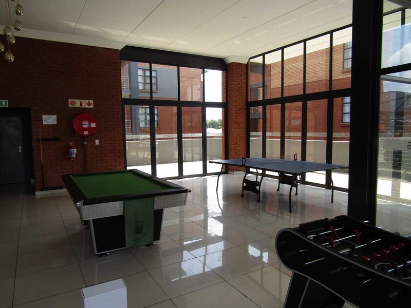 Spacious clubhouse area featuring exposed brick walls, large windows providing natural light, and tiled flooring, suitable for recreational activities.