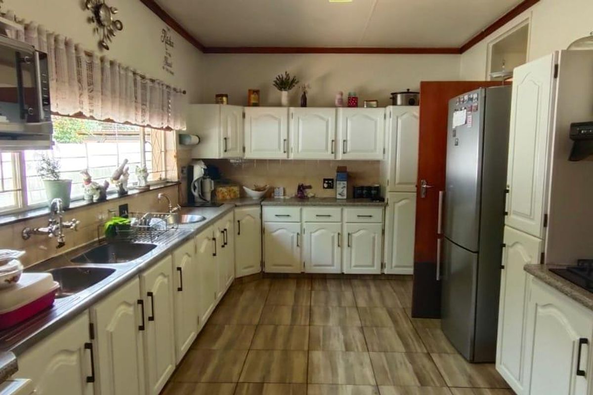 A functional kitchen featuring white cabinetry, tiled flooring, a gas hob with extractor fan, and a double sink with ample counter space.