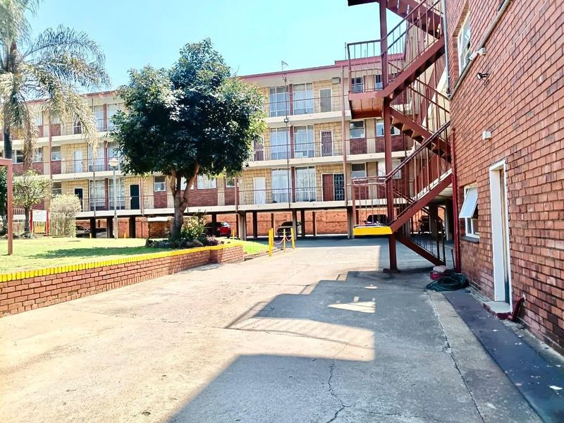 Exterior view of an apartment complex featuring a brick facade, external metal staircase, and a paved driveway area.
