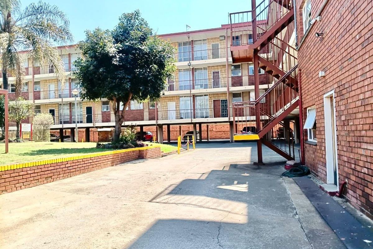 Exterior view of an apartment complex featuring a brick facade, external metal staircase, and a paved driveway area.