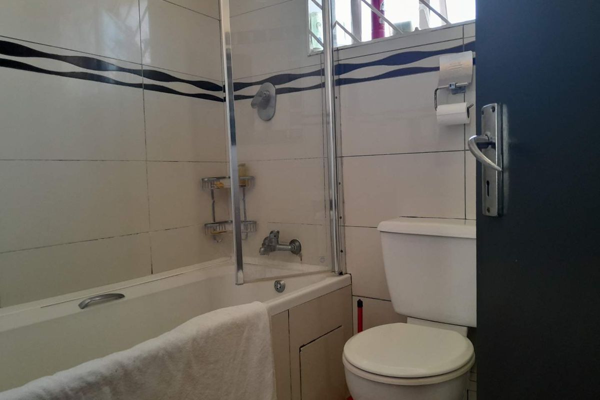 A functional bathroom featuring a bathtub with a glass shower screen, wall tiling, and a standard toilet.
