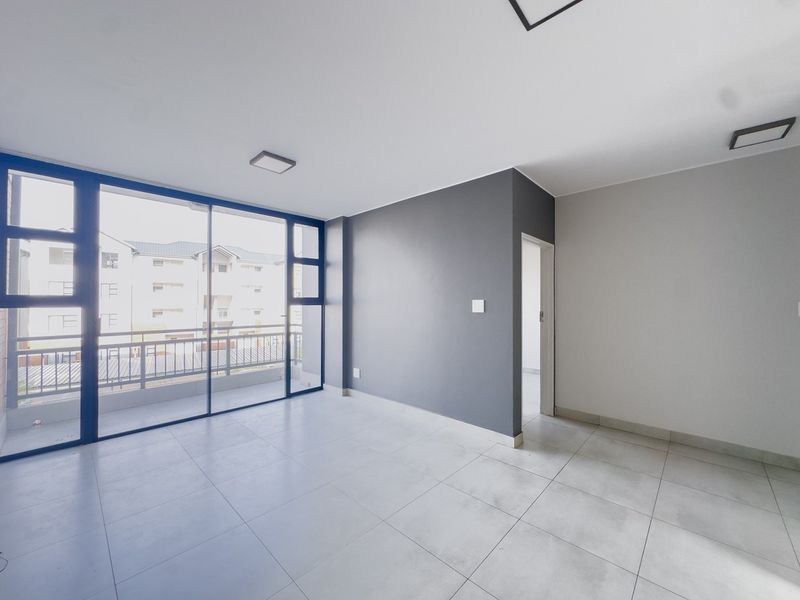 A bright, empty living area featuring large sliding glass doors leading to a balcony, neutral tiled flooring, and a modern grey accent wall.