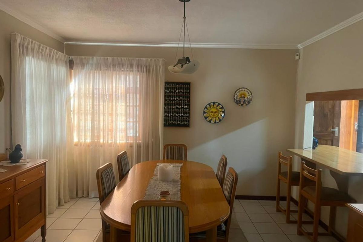 A dining room featuring tiled flooring, coving, and a pass-through window connecting to the adjacent kitchen area.