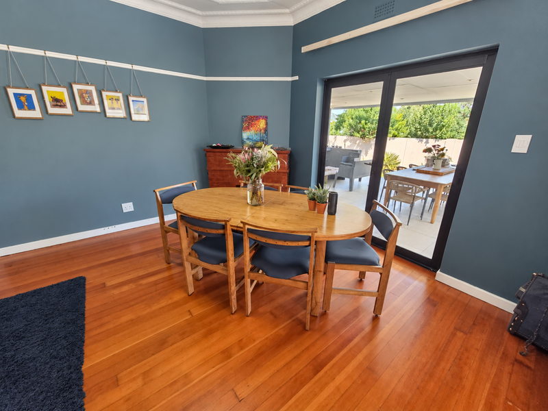 A well-maintained dining room featuring polished hardwood flooring, decorative crown molding, and large sliding glass doors that provide seamless access to the outdoor patio area.