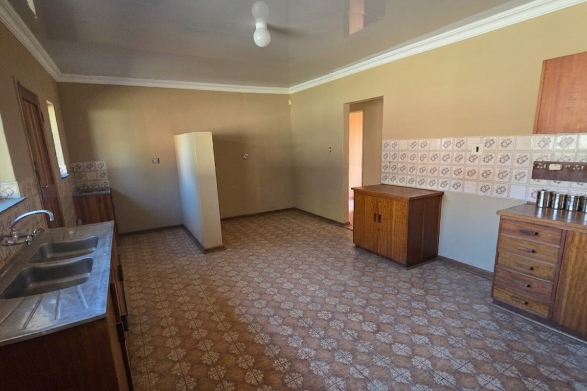 A functional kitchen space featuring wooden cabinetry, a double-basin stainless steel sink, and patterned floor tiles, offering a blank canvas for potential renovation.