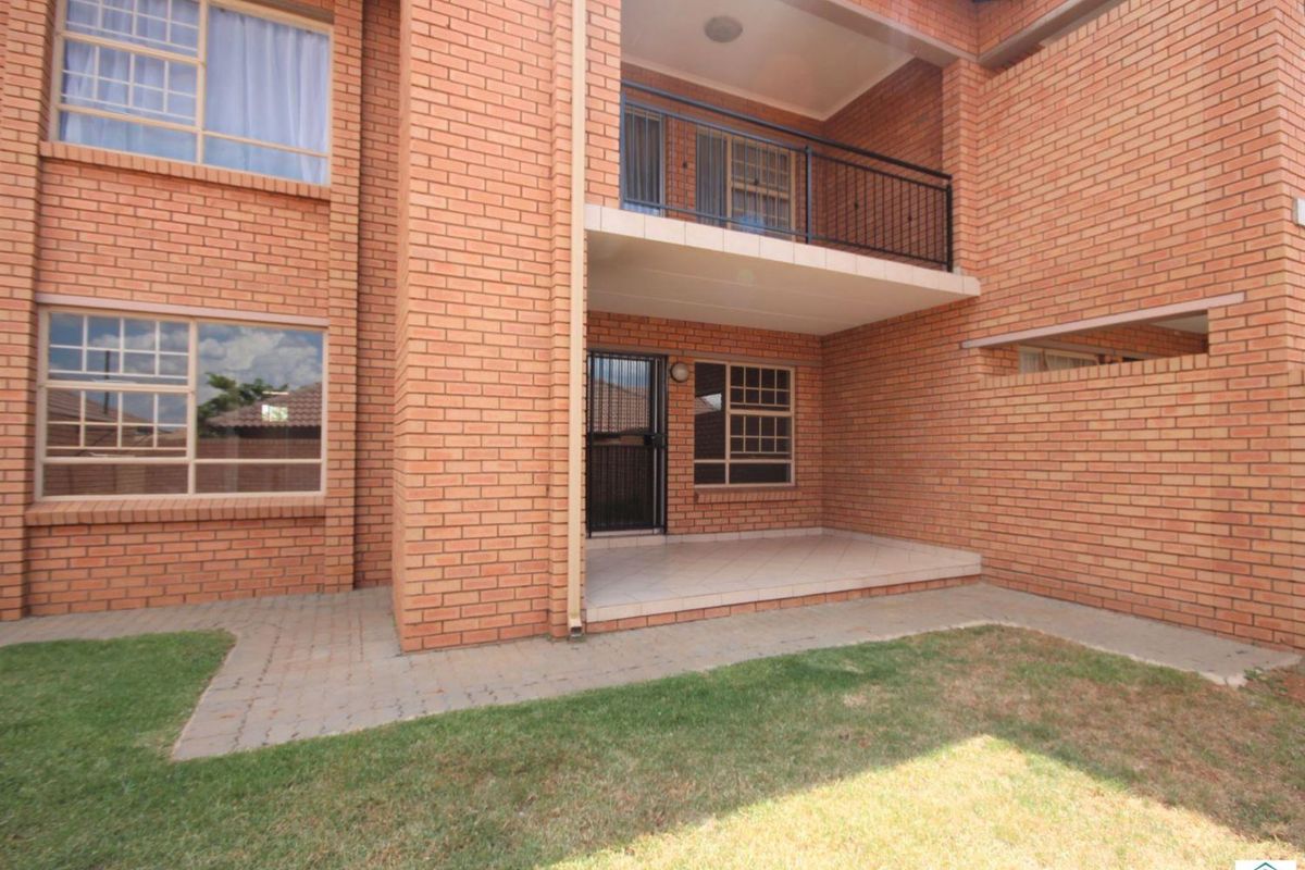 Exterior view of an apartment building featuring face brick facade, a ground floor patio, and an upper-level balcony with metal railings.