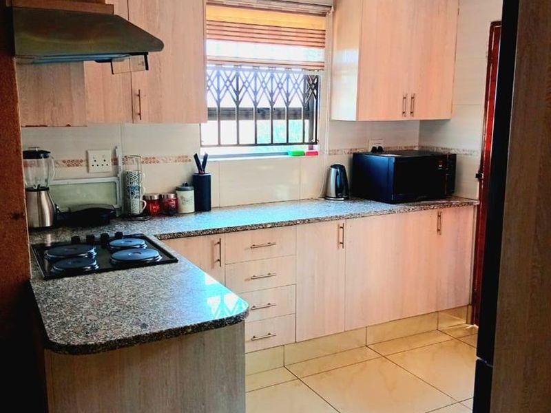 A functional kitchen featuring light wood-finish cabinetry, granite countertops, a gas hob with extractor fan, and neutral tiled flooring.