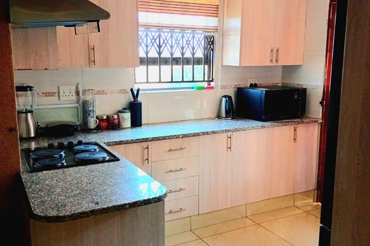 A functional kitchen featuring light wood-finish cabinetry, granite countertops, a gas hob with extractor fan, and neutral tiled flooring.