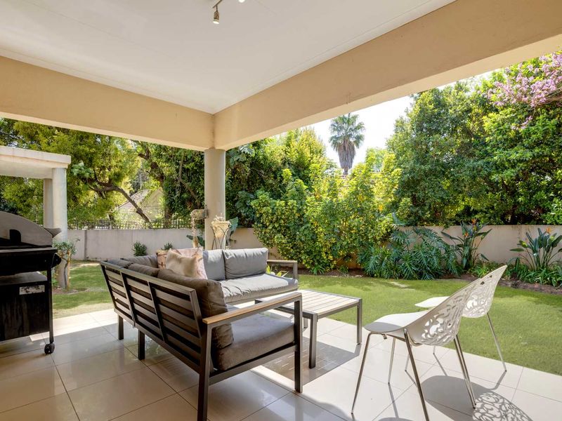 A covered outdoor patio featuring tiled flooring and a concrete support column, overlooking a private garden with established greenery and boundary walls.