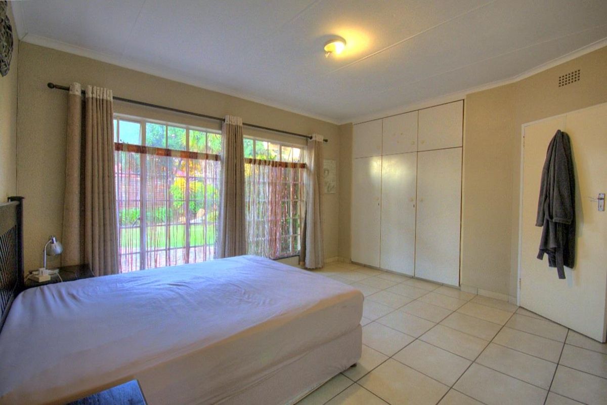 A spacious bedroom featuring large windows with garden views, tiled flooring, and extensive built-in wardrobe storage.