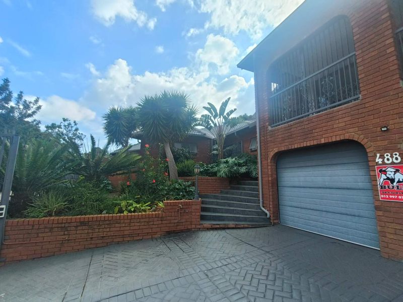 Front elevation of a brick house featuring a paved driveway, integrated garage, and a landscaped garden with a tiled staircase leading to the entrance.