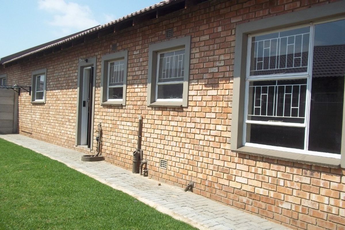 Rear exterior view of the townhouse featuring a face brick facade, paved walkway, and security bars on the windows.