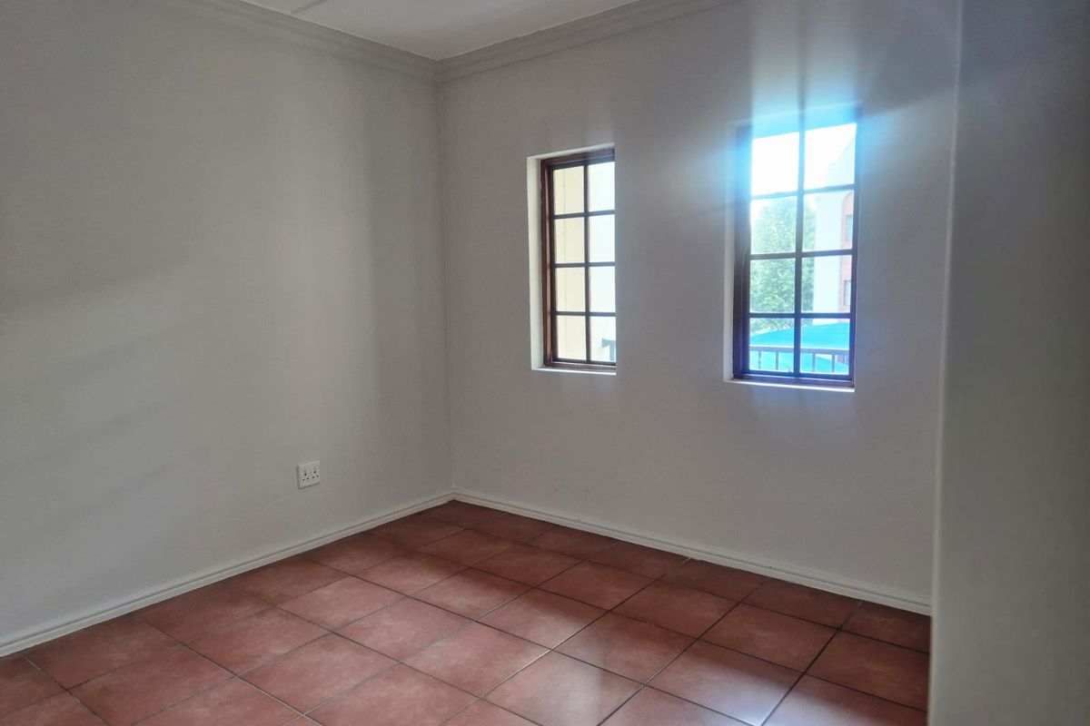 An empty bedroom featuring tiled flooring, neutral walls, and two windows with wooden frames, providing a blank canvas for personalization.