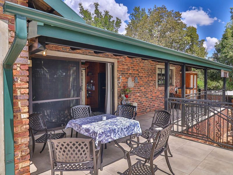 A spacious covered patio featuring exposed brick walls, tiled flooring, and a decorative wrought iron railing, providing a comfortable outdoor living space.