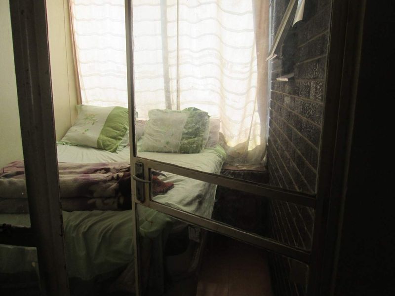 A compact bedroom featuring an exposed brick wall and a sliding glass door entrance, requiring cosmetic updates to improve its overall condition.