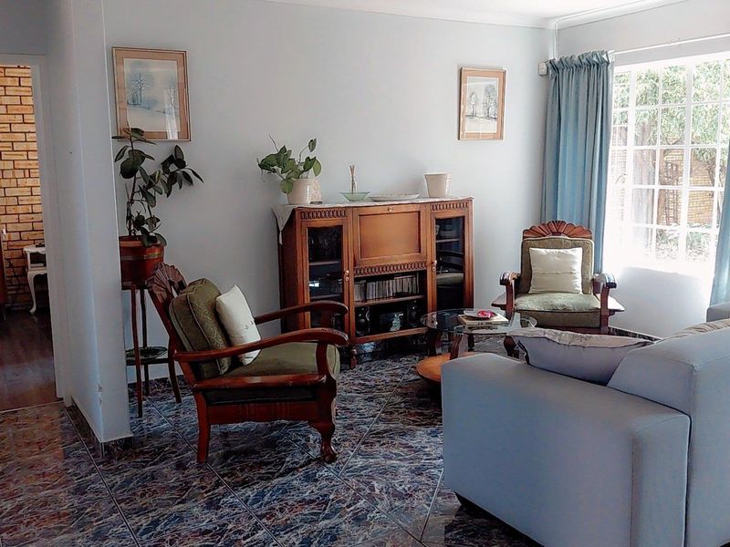 A comfortable living room featuring tiled flooring, a large window for natural light, and an adjacent area with an exposed brick wall.
