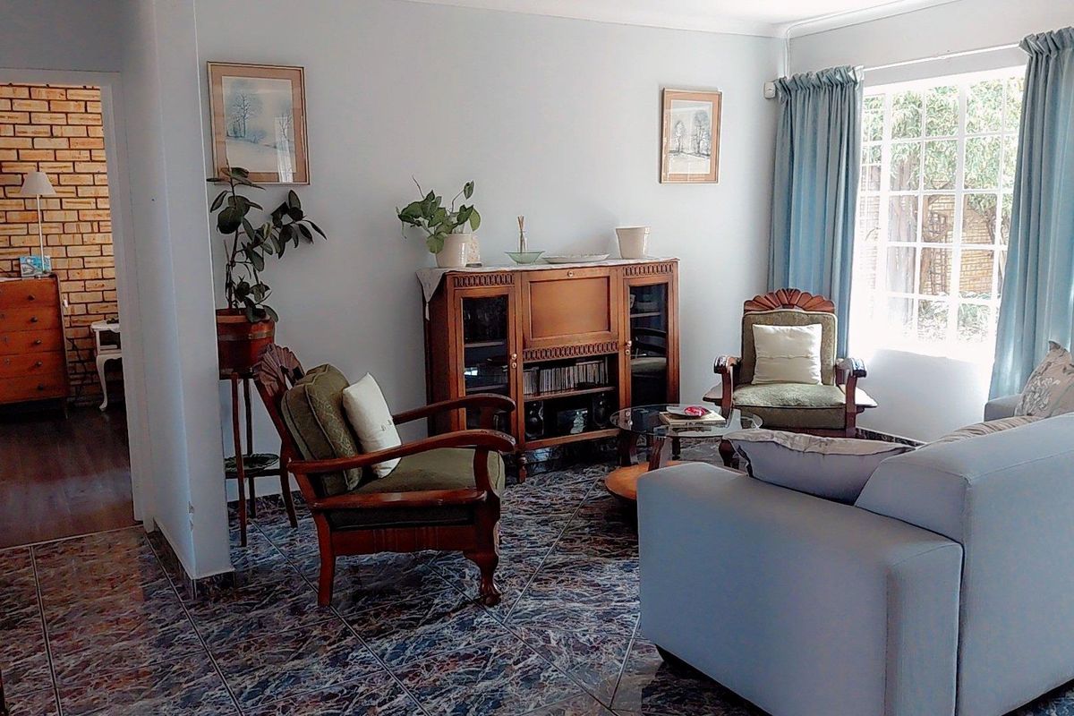 A comfortable living room featuring tiled flooring, a large window for natural light, and an adjacent area with an exposed brick wall.