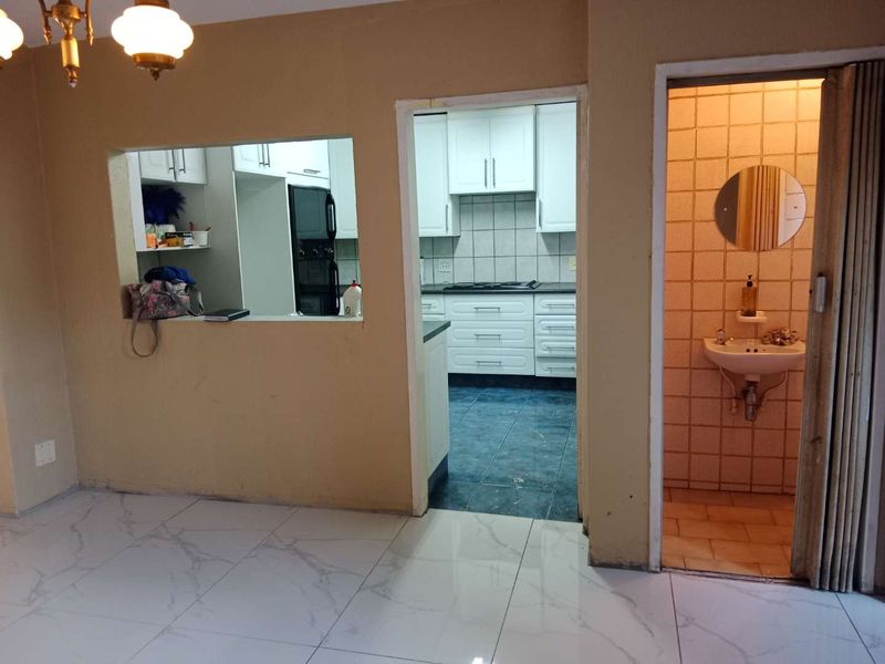 Open plan living area featuring a serving hatch to the kitchen, tiled flooring, and an adjacent guest bathroom with a wall-mounted basin.