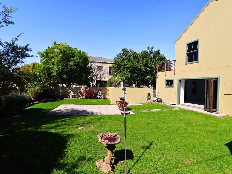 Rear view of the property featuring a well-maintained lawn, paved patio area, and access to the interior through folding glass doors.