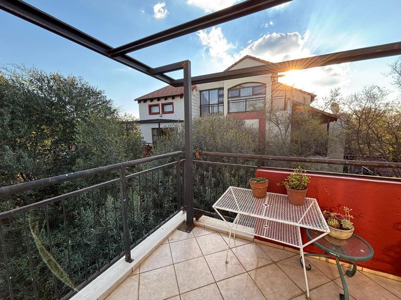 A private balcony featuring tiled flooring, a metal balustrade, and a structural pergola frame, offering an outdoor space with views of the surrounding property.