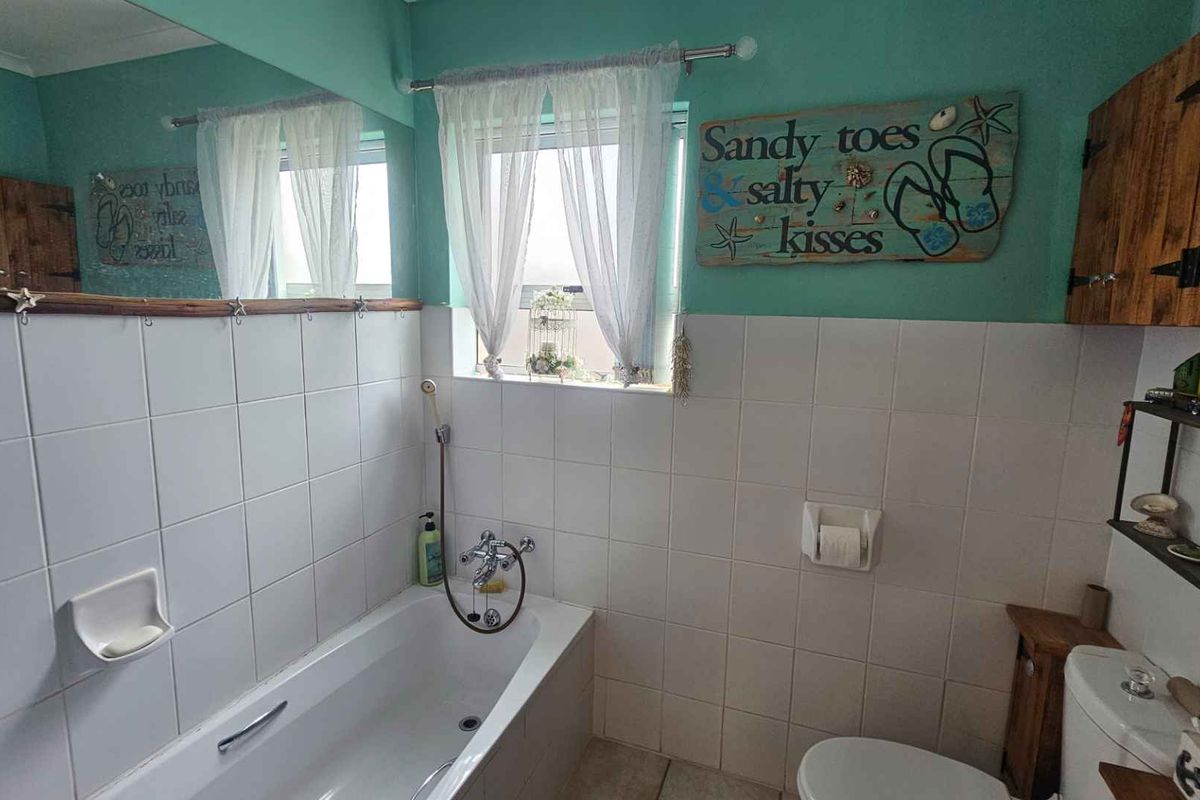 A functional bathroom featuring a built-in bathtub with shower mixer, wall-mounted toilet, and large vanity mirror with tiled splashbacks.