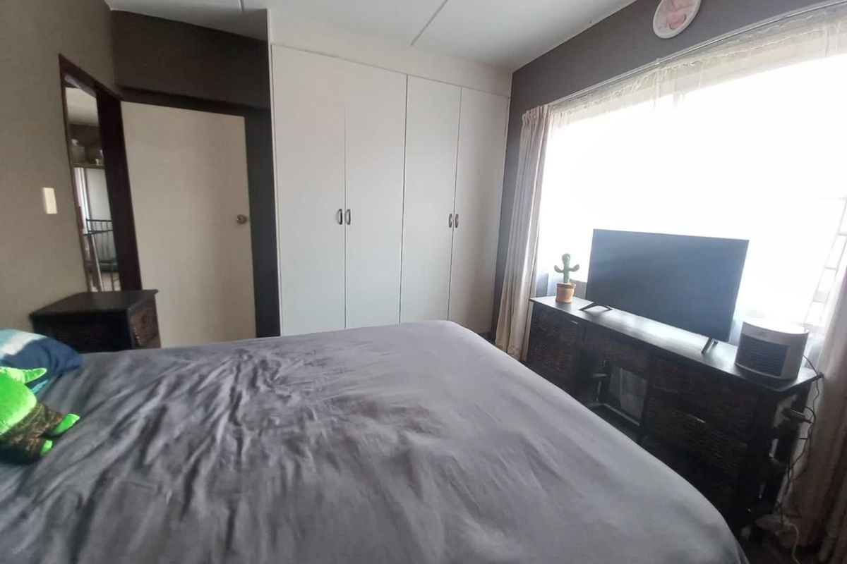 A bedroom featuring built-in cupboards and a large window allowing for natural light.