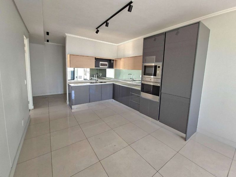 Modern kitchen featuring sleek grey cabinetry, built-in oven and microwave, mirror splashback, and tiled flooring in an open-plan layout.
