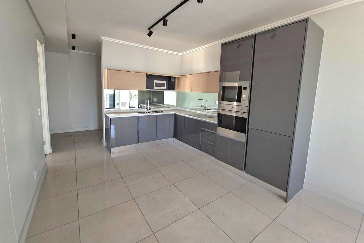 Modern kitchen featuring sleek grey cabinetry, built-in oven and microwave, mirror splashback, and tiled flooring in an open-plan layout.