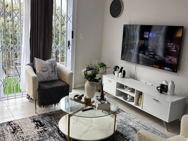 A well-maintained living room featuring tiled flooring and a sliding glass door with a security gate, providing access to the outdoor area.