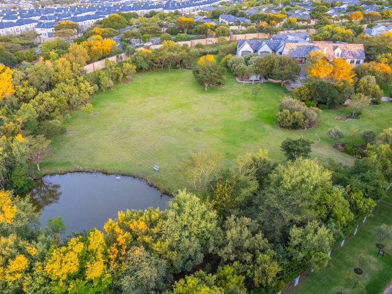 An aerial view of a spacious residential plot featuring a large manicured lawn, mature trees, and a private pond.