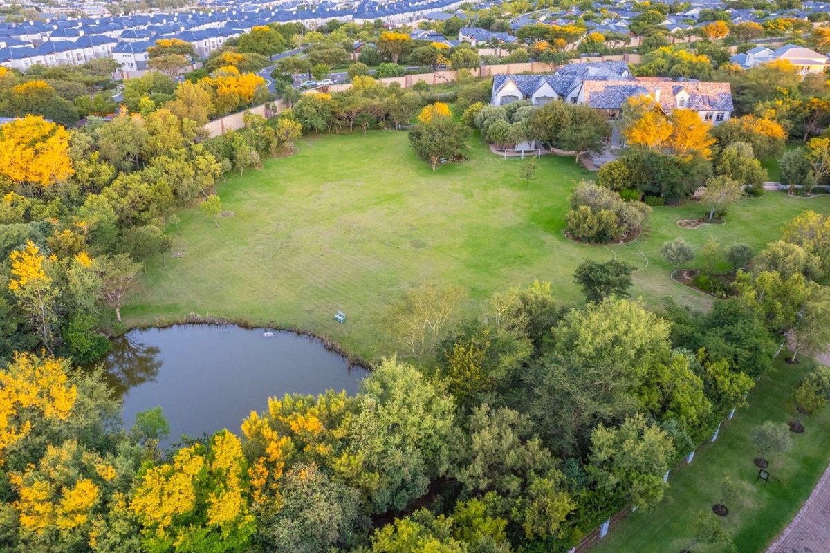 An aerial view of a spacious residential plot featuring a large manicured lawn, mature trees, and a private pond.